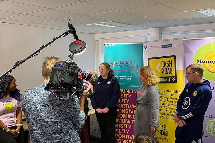 women being interviewed for STV in front of banner stands with logos on them